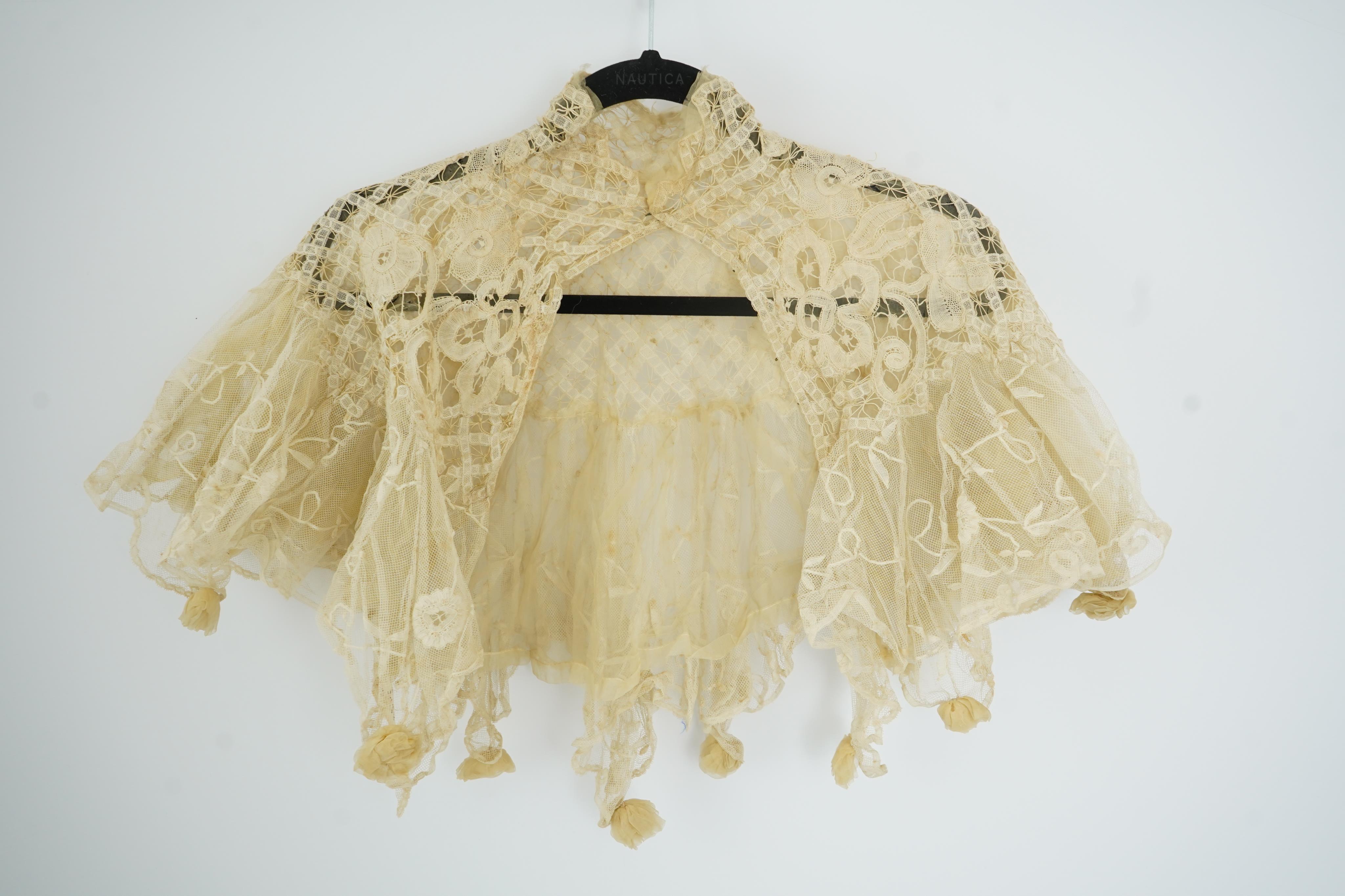 An Edwardian high collared cream tape lace wedding over blouse, made with a deep net frill and cream chiffon rose detail hanging from lower edge, top of collar to rose detail at the front 46cm. Condition - fine silk chif